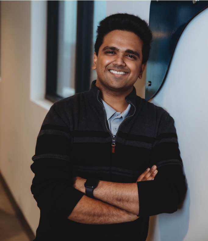 Person smiling and leaning against wall with arms folded