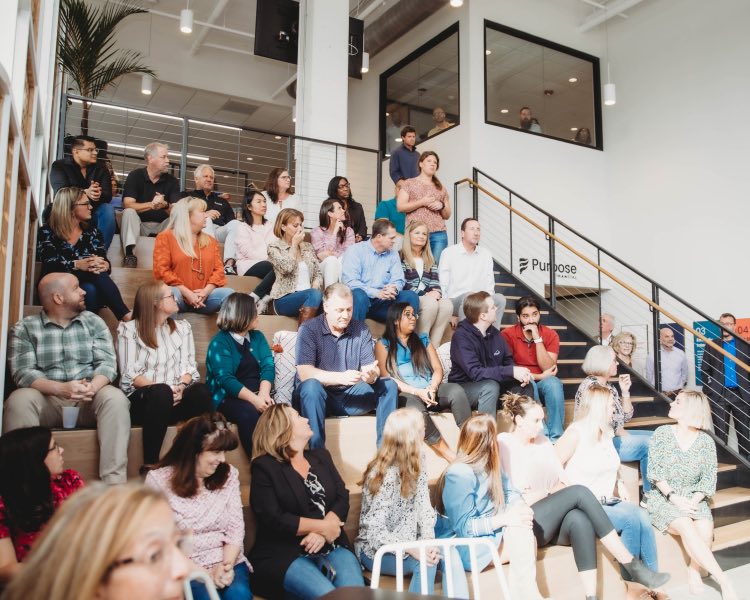 Group photo of large team of Purpose Financial employees sitting on and around the steps inside our office